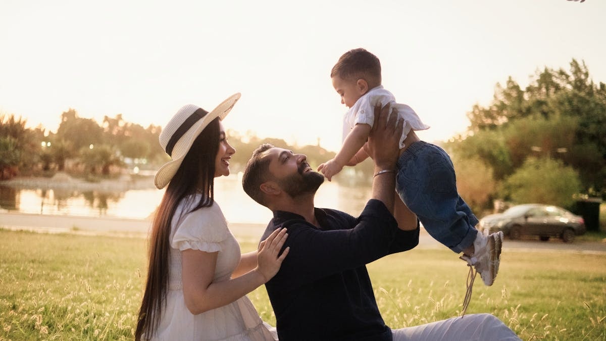 A joyful family moment with parents and child in a sunny park setting.